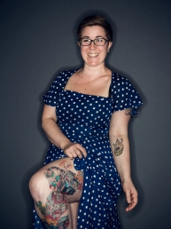 Emma Berlin in blue dress with white dots. Showing leg with tattoos.