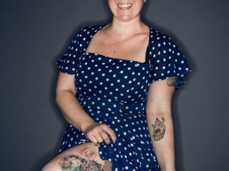 Emma Berlin in blue dress with white dots. Showing leg with tattoos.